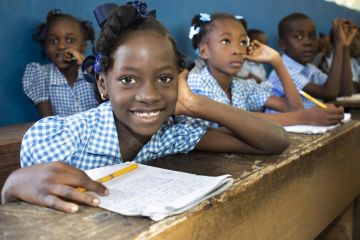 Meisje lachend in schoolbank met schriftje